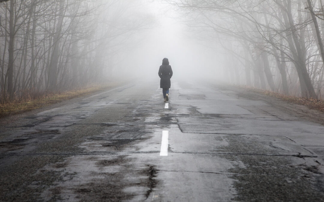 Lonly woman  walk away into the misty foggy road in a dramatic mystic scene.